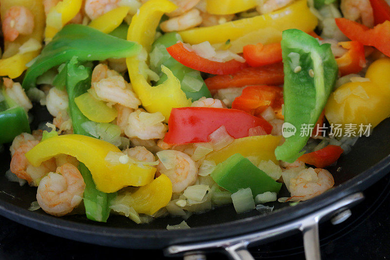 健康饮食食品的形象，东方大虾海鲜炒冻大虾/虾，切碎的洋葱丁，交通灯辣椒辣椒蔬菜，红的，黄的，绿的切片，炒晚餐的饭菜被煮在大的不干胶煎锅